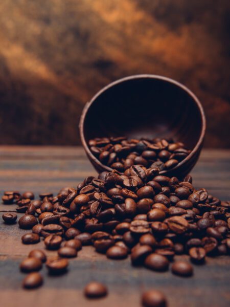 Chicchi di caffè tostati che fuoriescono da una ciotola in legno su un tavolo rustico, con sfondo caldo e sfocato.